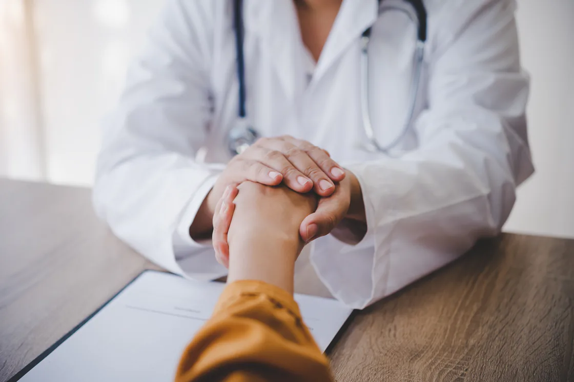 Un médecin en blouse blanche tient la main d'un patient lors d'une consultation